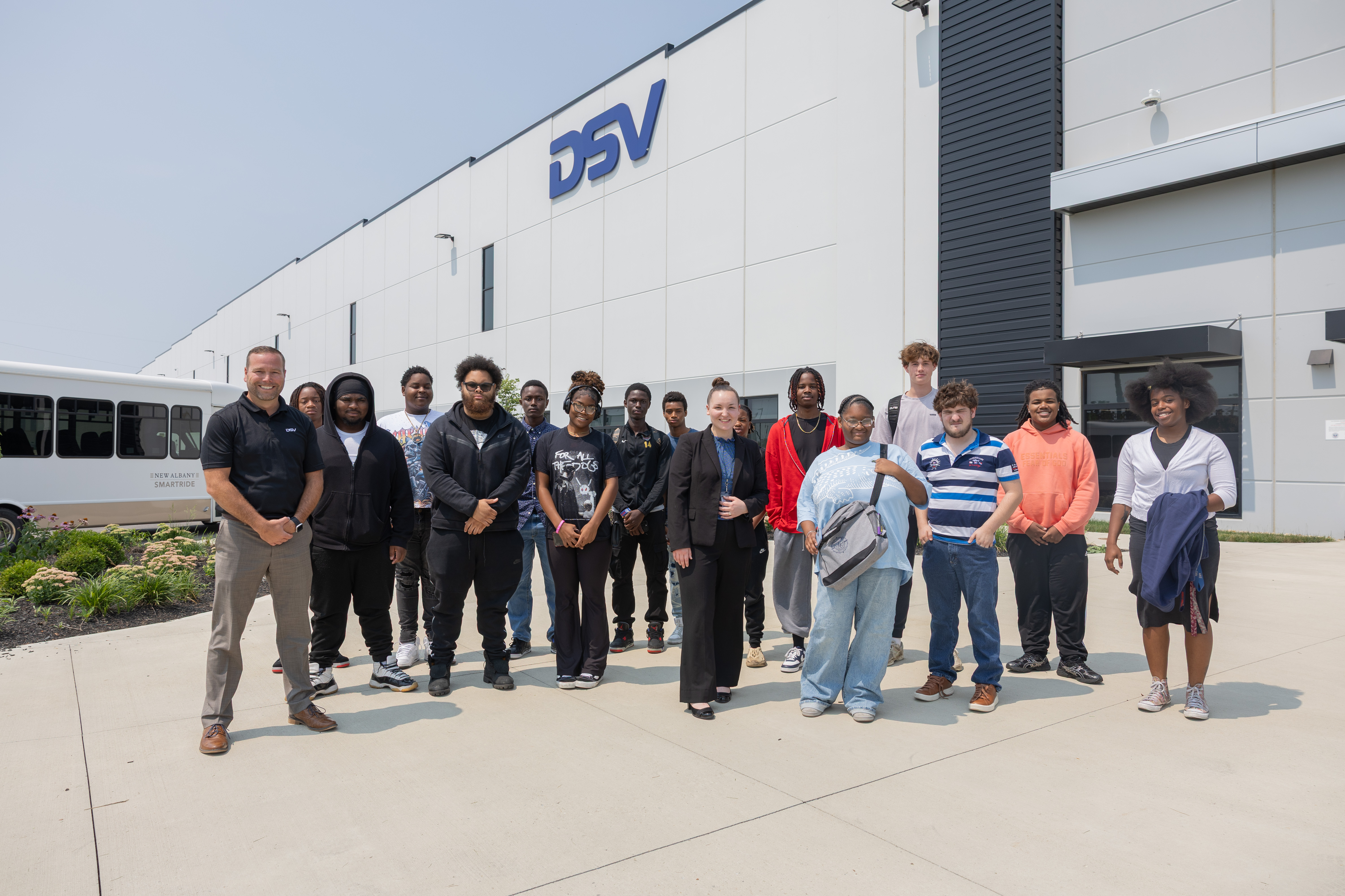 A group of students stand in front of a big white building with a "DSV" logo on it.