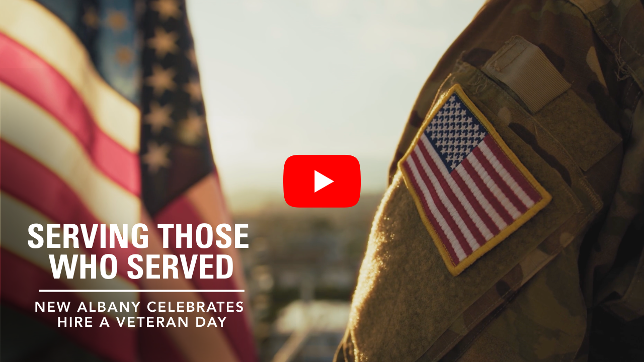 A military member standing in front of an american flag with a Youtube Play button in the center